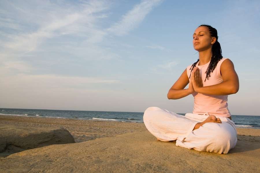 Une femme en méditation sur une plage pratique la respiration yogique au lever du soleil.