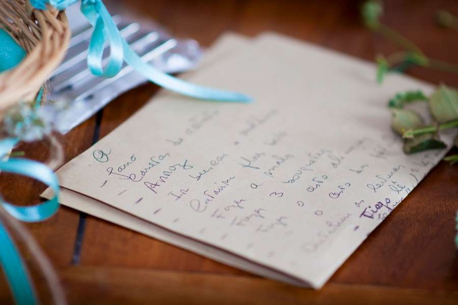 Un aperçu rapproché d'une liste des invités manuscrite posée sur une table en bois, accompagnée d'un ruban bleu clair et de détails végétaux.