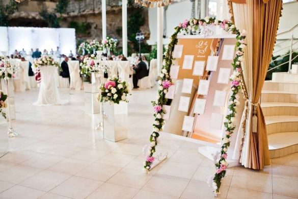 Un grand panneau affichant la liste des invités et le plan de table, richement décoré de fleurs et installé dans une salle de réception élégante.