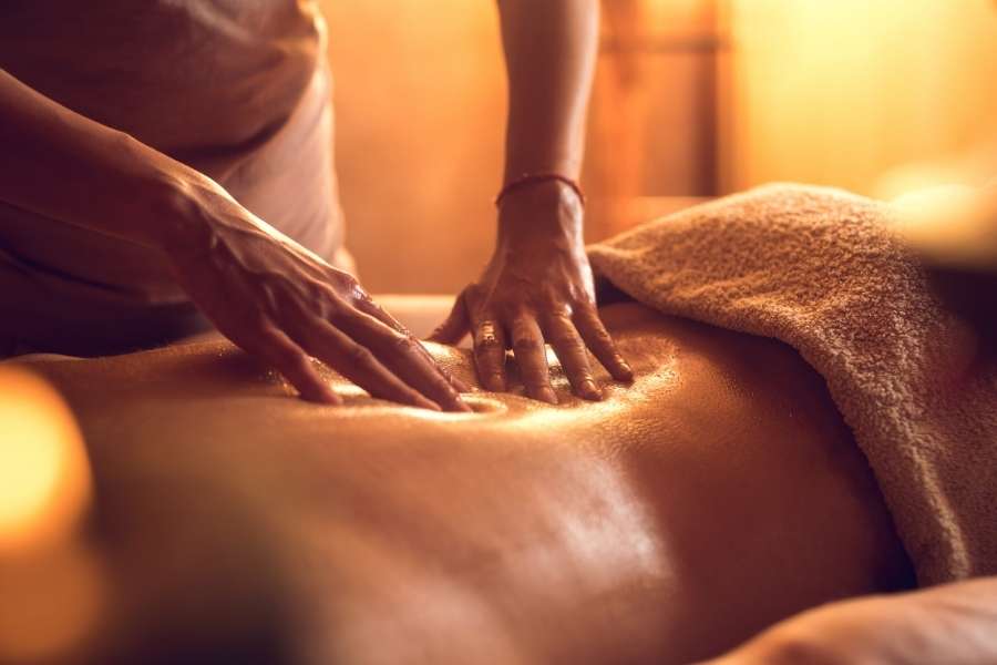 Un masseur applique une pression ferme et glissante sur le dos huilé d'un client dans une lumière chaude.