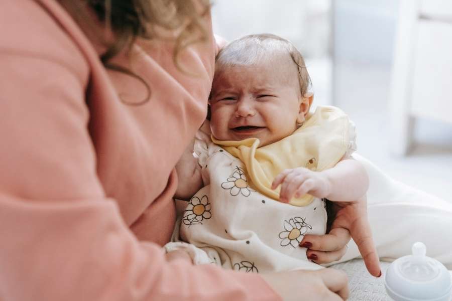 Un bébé qui pleure dans les bras de sa mère en comprenant les types de pleurs.