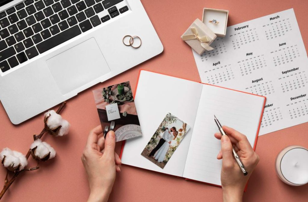 Vue du dessus de mains organisant des tirages et un carnet pour apprendre comment composer son album photo de mariage près d'un ordinateur portable
