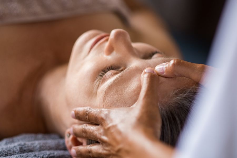 Praticienne effectuant des pressions ciblées pour détendre les traits de son visage grâce au massage facial anti-âge.   